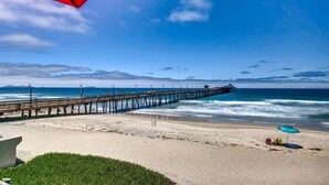 Una playa con un muelle de madera que se adentra en el océano, una sombrilla roja y una sombrilla azul en la arena.