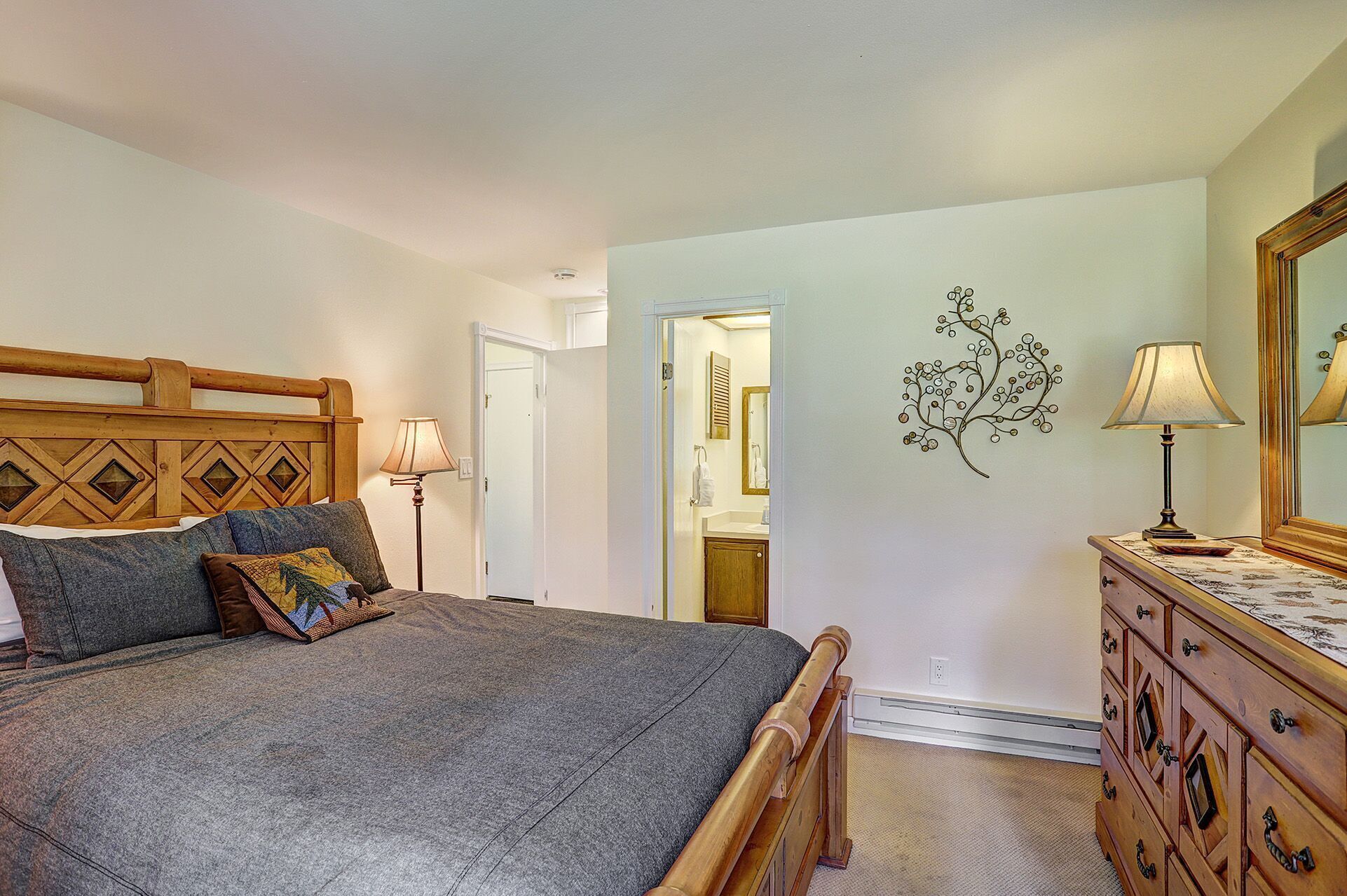 A bedroom with a bed, dresser, and a wall-mounted lamp.