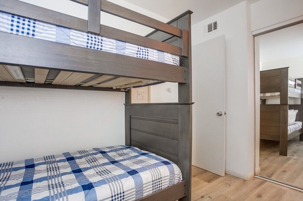 Un lit superposé avec un matelas à carreaux, une tête de lit en bois et une porte blanche avec un miroir.