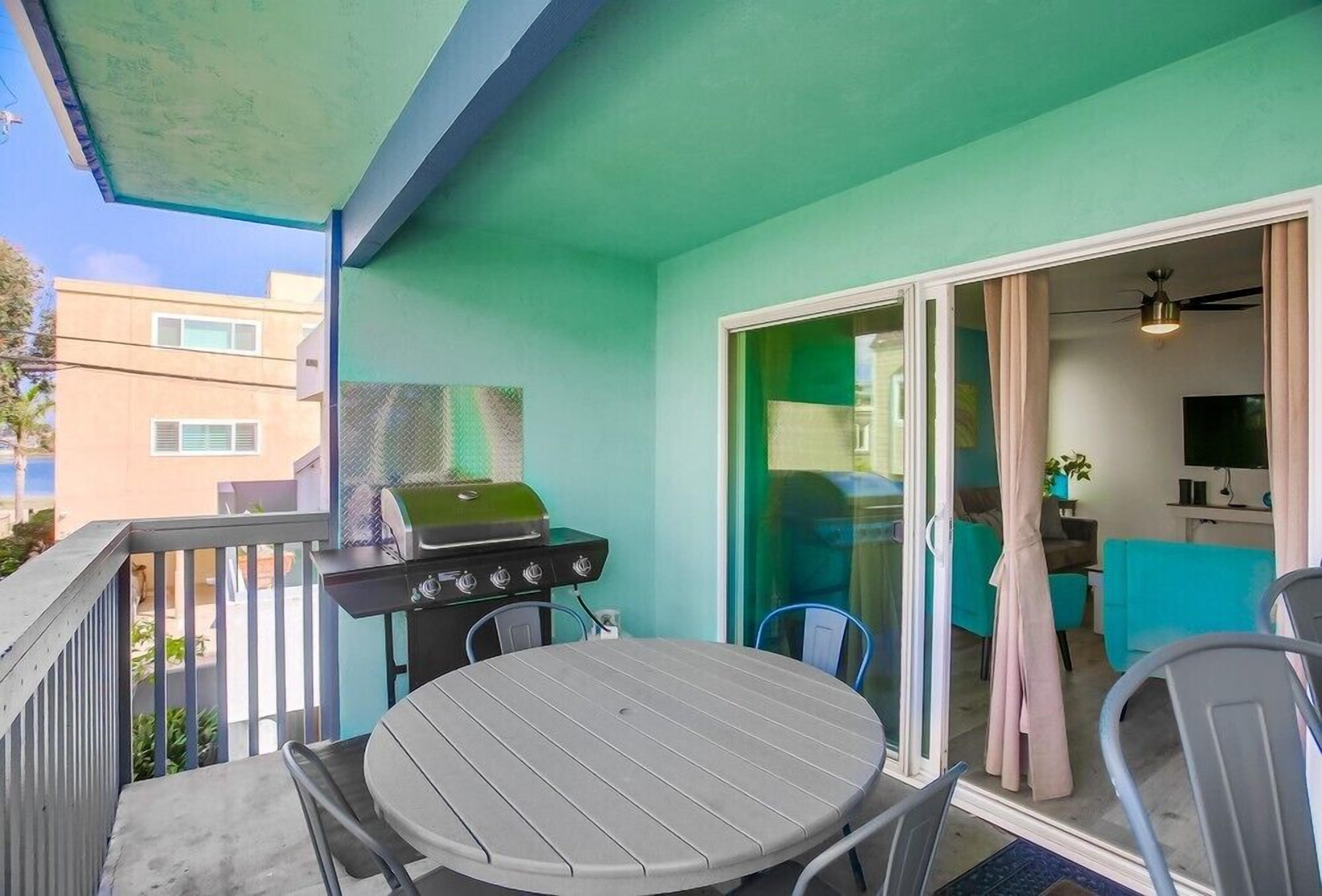 A balcony with a grill, a table, and chairs.