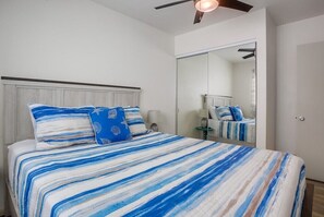 A bedroom with a bed, a ceiling fan, a mirror, and a nightstand.