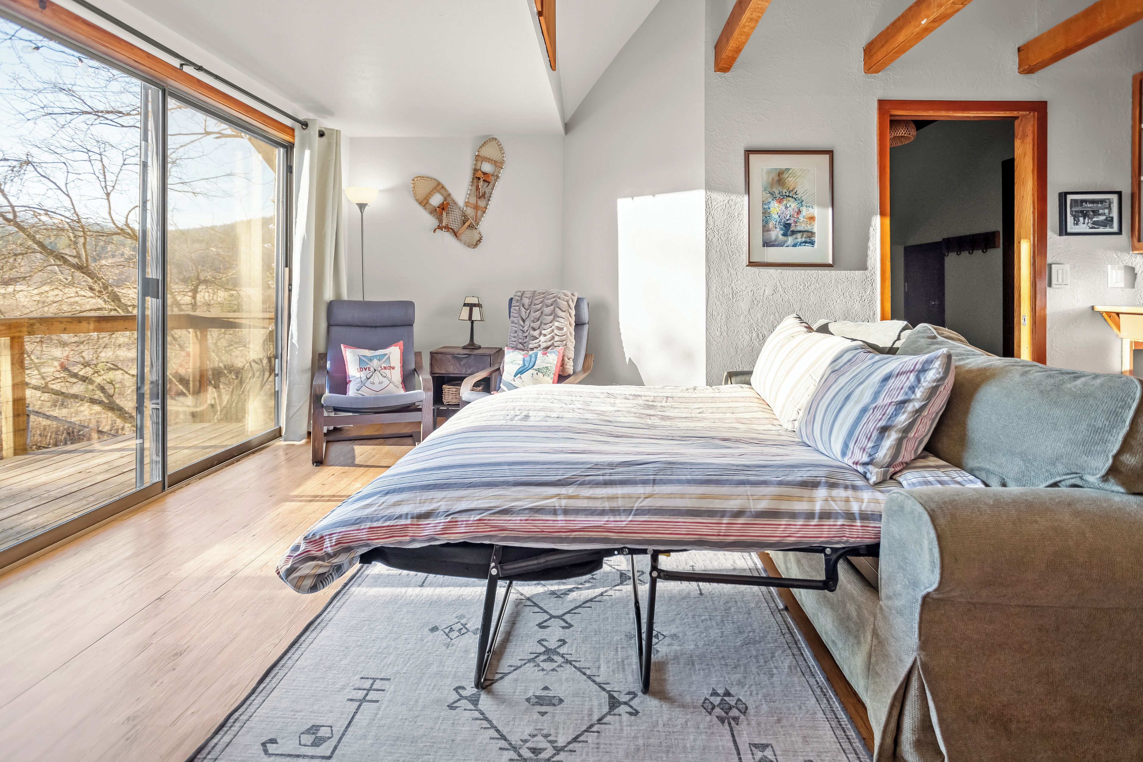 Ein Schlafzimmer mit großem Fenster, einem Bett mit gestreifter Bettwäsche, einem Sessel und einem kleinen Tisch mit Lampe.