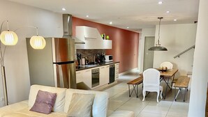 A modern living room with a sofa, a dining table with chairs, a kitchen area with appliances, and a staircase. - Walking distance to the beach, bars & restaurants. 3 bed/3 bath condo with pool! (Noord)