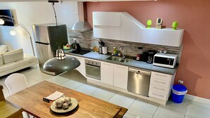 A modern kitchen with white cabinets, a stainless steel refrigerator, a microwave, and a dishwasher. There is a dining table with chairs and a lamp. - Walking distance to the beach, bars & restaurants. 3 bed/3 bath condo with pool! (Noord)