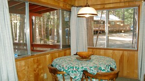 A wooden dining area with a table covered by a floral tablecloth, two wooden chairs, and a hanging light fixture. - (28) Raccoon's End at The Redwoods In Yosemite (Yosemite National Park)