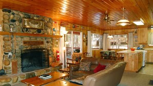 A cozy cabin interior with a stone fireplace, leather furniture, and a kitchen area. - (28) Raccoon's End at The Redwoods In Yosemite (Yosemite National Park)