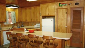 A kitchen with wooden cabinets, a white refrigerator, a microwave, and a red pot on the counter. There are four wooden bar stools. - (28) Raccoon's End at The Redwoods In Yosemite (Yosemite National Park)