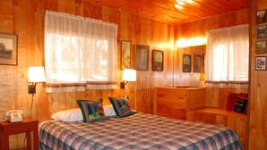 A wooden cabin room with a bed, bedside lamps, a small table, and a bench. - (28) Raccoon's End at The Redwoods In Yosemite (Yosemite National Park)