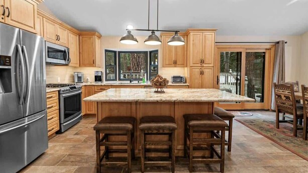 A modern kitchen with wooden cabinets, stainless steel appliances, and a central island with bar stools. - Walk to Summit, Spa, BBQ, Fireplace (Big Bear)