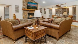 A cozy living room with a stone fireplace, leather sofas, a wooden coffee table, and a large window with blinds. - Walk to Summit, Spa, BBQ, Fireplace (Big Bear)