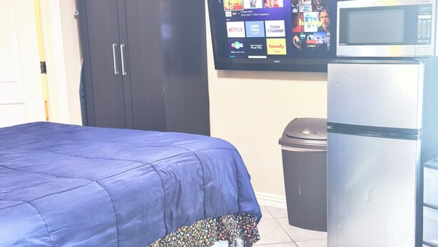 A room with a bed, a TV, a refrigerator, and a trash bin.