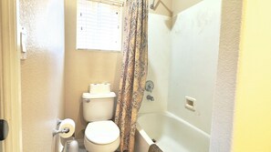 Een badkamer met een toilet, toiletpapier, een douchegordijn en een bad.