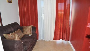Ein Wohnzimmer mit einem dunkelbraunen Sofa, zwei gemusterten Kissen und roten Vorhängen.