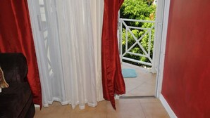 Ein Zimmer mit einem dunkelbraunen Sofa, einem weißen Vorhang und Blick auf ein weißes Tor, das zu einem grünen Außenbereich führt.