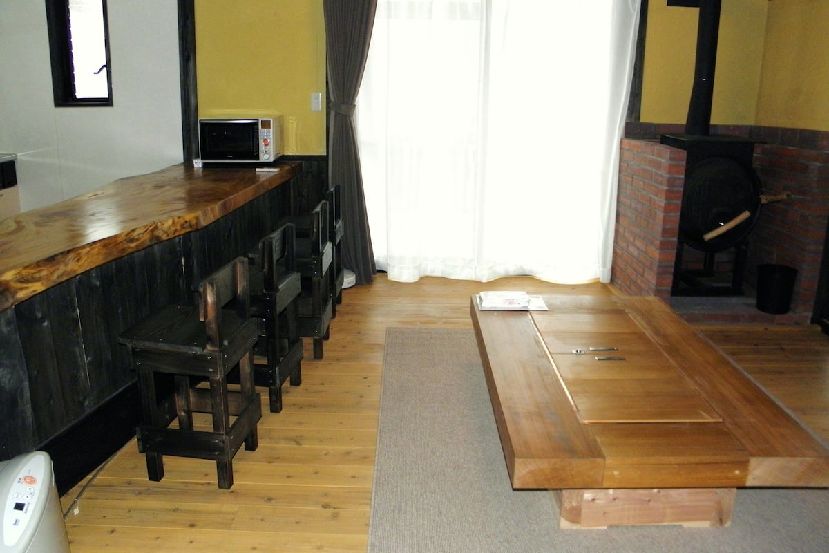 A room with a wooden bar counter, chairs, a microwave, a fireplace, and a large window with curtains.