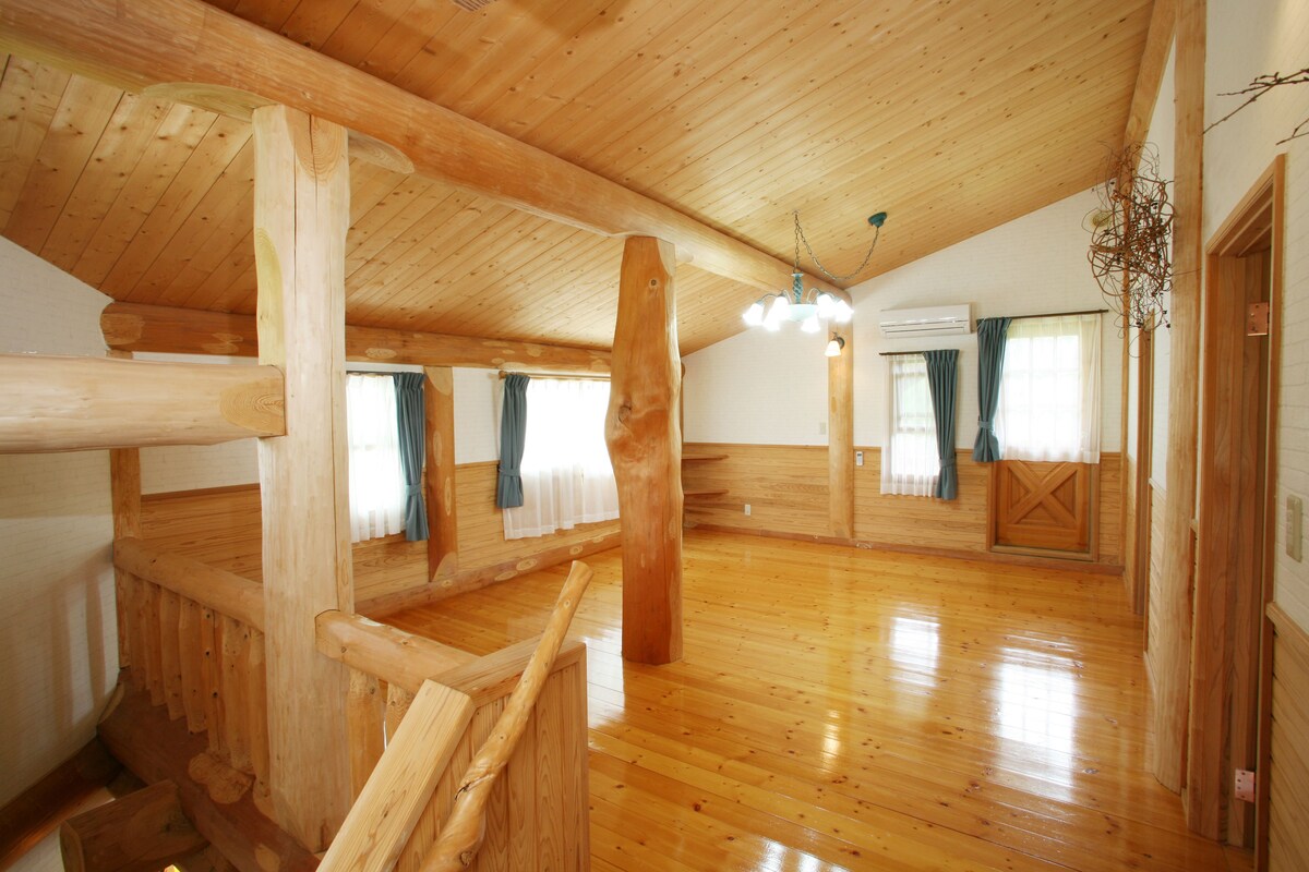 A spacious room with wooden floors and a sloped ceiling, featuring a wooden railing and a hanging light fixture.