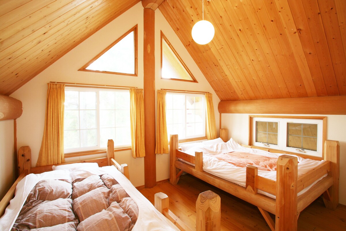 A cozy attic bedroom with two wooden beds, large windows, and a sloped ceiling.