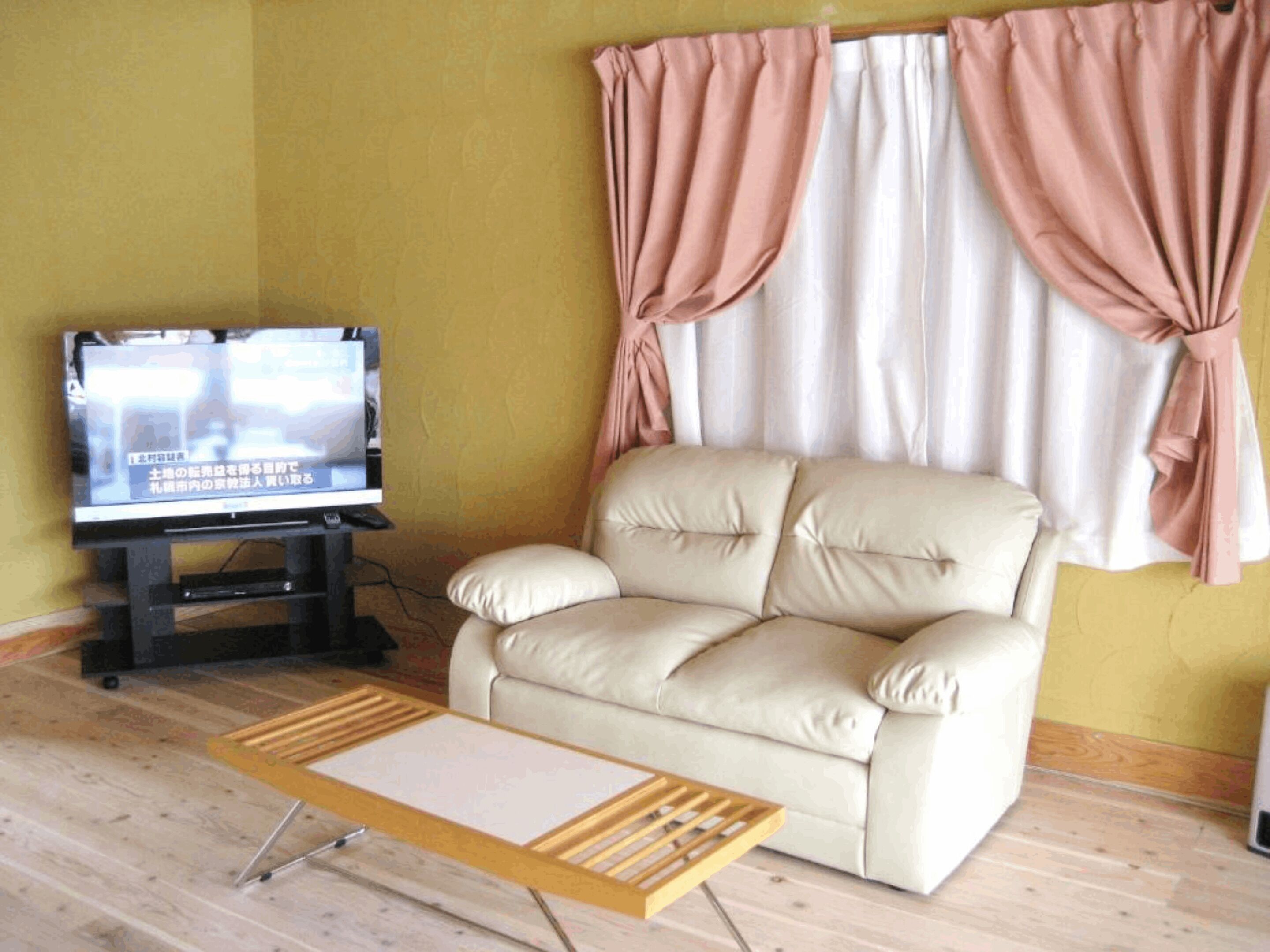 Un salon avec un canapé beige, un téléviseur posé sur un meuble et une table basse en bois.