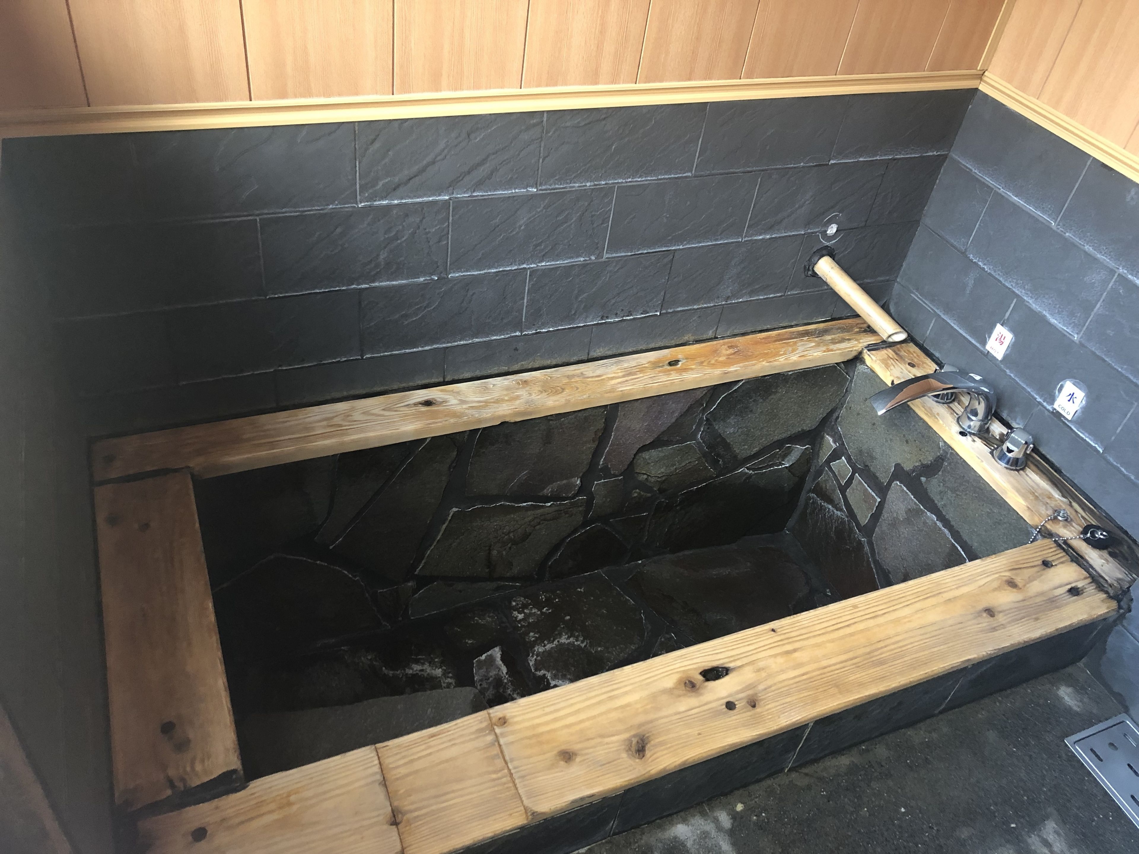 Een bad met houten omlijsting, zwarte steentjes en een houten bankje.