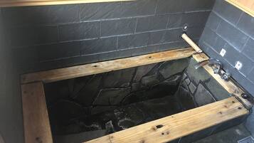 Een bad met houten omlijsting, zwarte steentjes en een houten bankje.