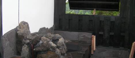 Ein Steinelement mit Wasserspeil, eine Holzbank und eine Holzhütte mit Fenster.