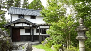 Et traditionelt japansk hus med et tagtækket tag, en træterrasse og en stenen lanterne i haven.