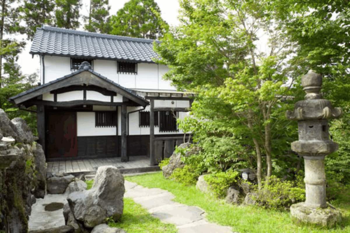 A traditional Japanese house with a tiled roof, a wooden porch, and a stone lantern in the garden.