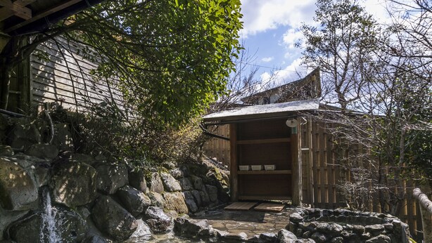En traditionel japansk bygning med træfacade, en stenfountain og en klar himmel.