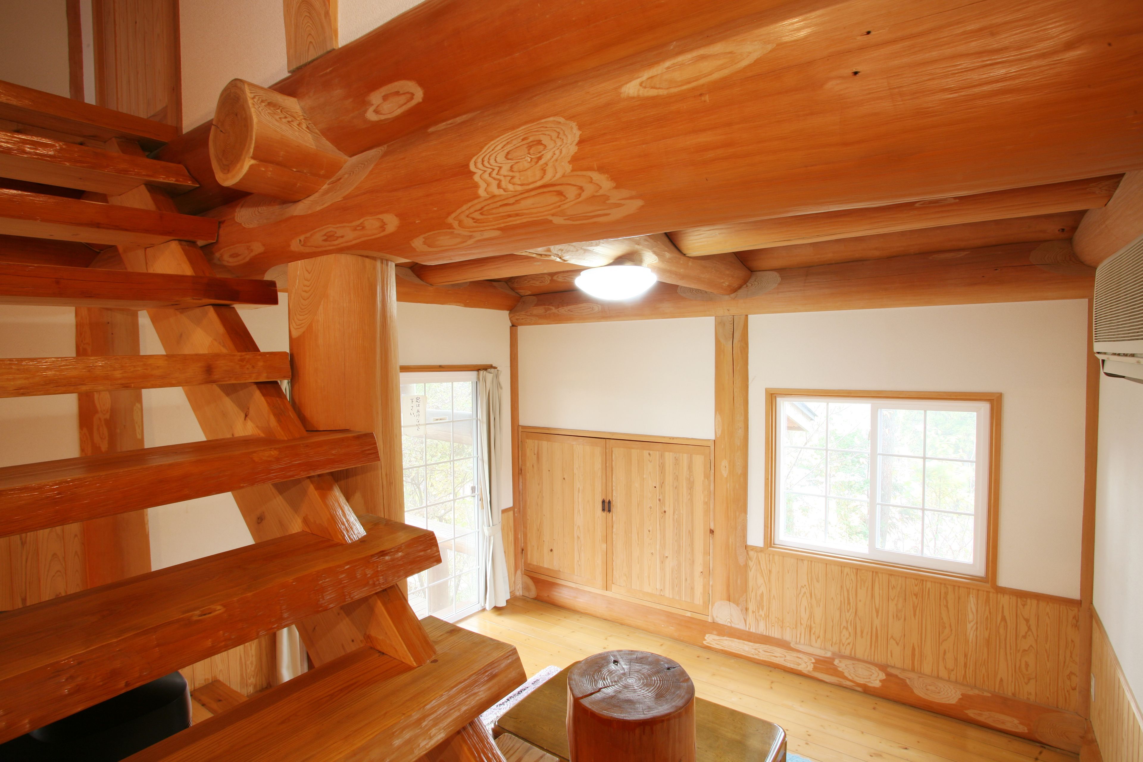A wooden interior with a staircase, wooden walls, and two windows.