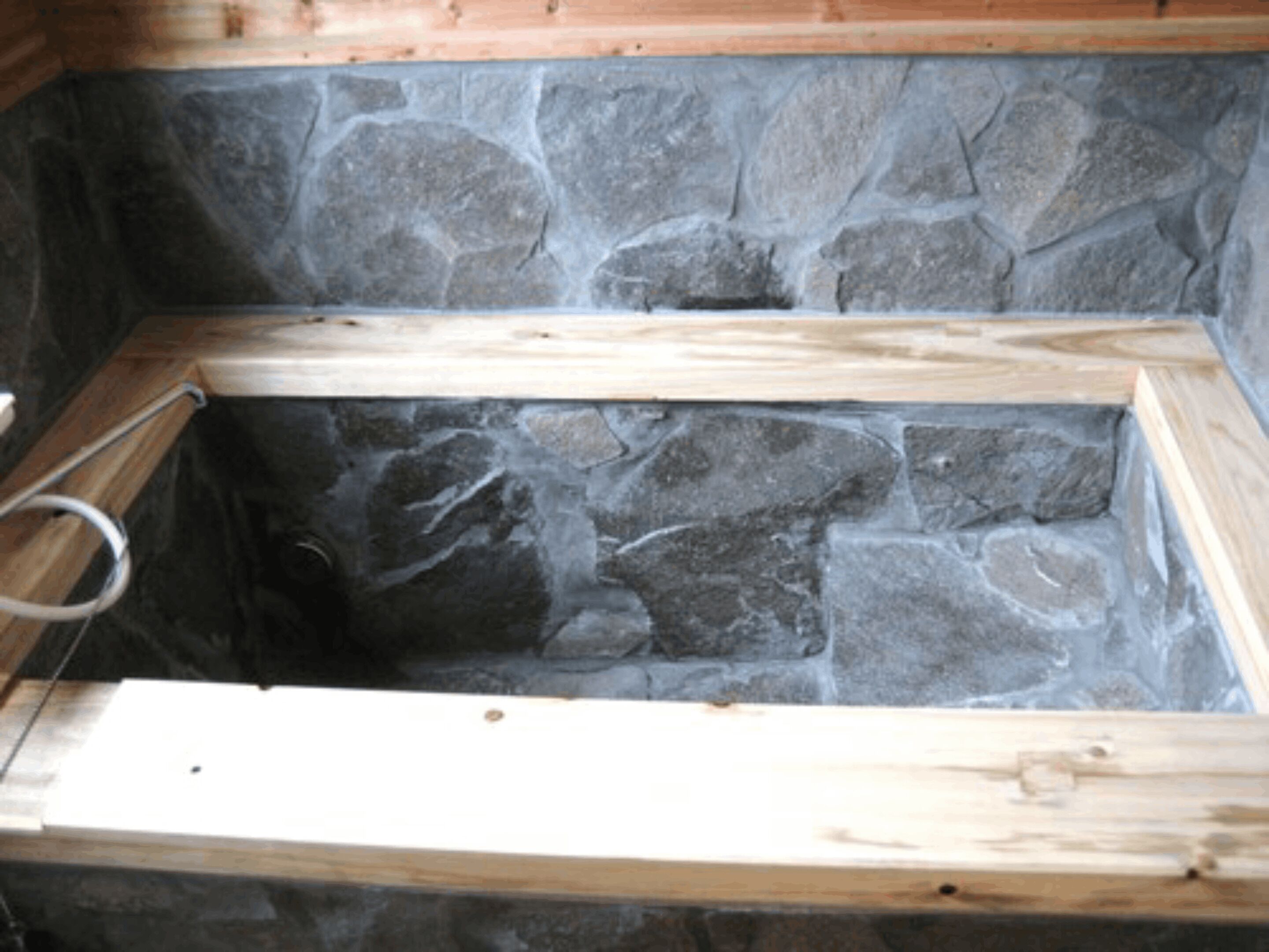 A stone-walled room with wooden beams and a metal ring.