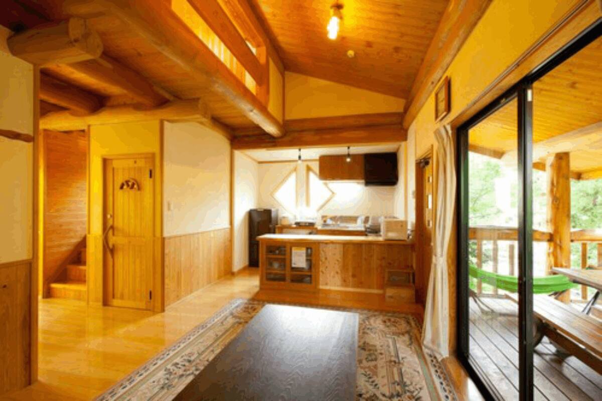 A wooden interior with a kitchen area, a staircase, and a large sliding glass door leading to an outdoor deck.
