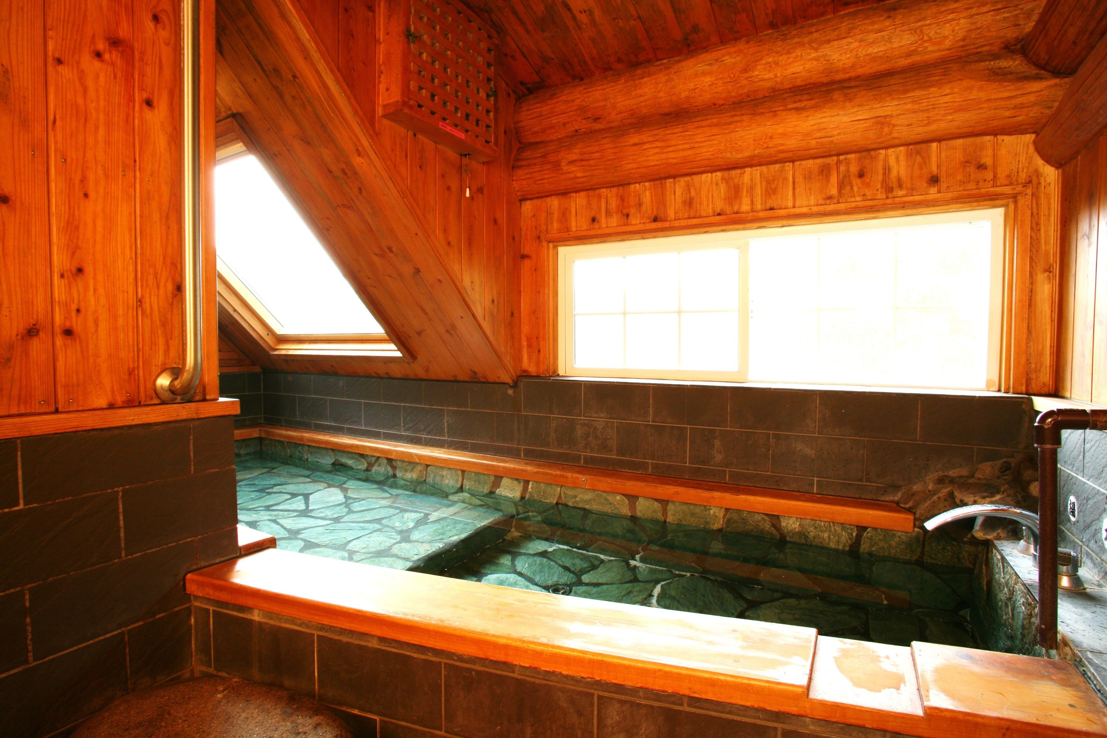 A wooden cabin interior with a stone-lined hot tub, a window, and a skylight.
