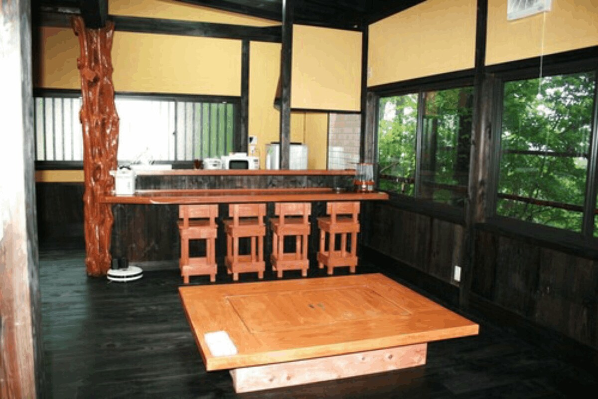 A traditional Japanese-style room with tatami flooring, a low wooden table, and a view of greenery through large windows.