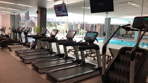 A gym with multiple treadmills, a pool, and large windows. - Old Town Scottsdale - Optima Camelview - Modern/Furnished, Walk To All Amenities (Scottsdale)