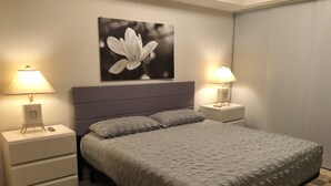 A neatly made bed with a grey headboard, two bedside tables with lamps, a large wall-mounted picture of a flower, and a patterned rug. - Old Town Scottsdale - Optima Camelview - Modern/Furnished, Walk To All Amenities (Scottsdale)
