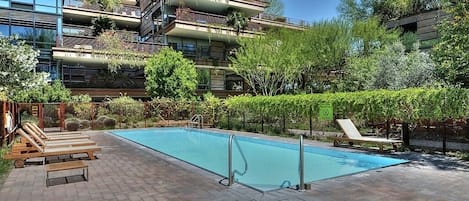 Un moderno edificio de apartamentos con jardín en la azotea, piscina y mobiliario de exterior.