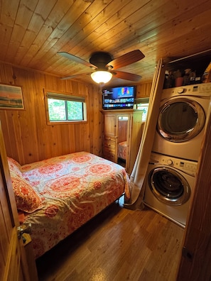 A compact room with a bed, a ceiling fan, a television, and a washing machine.