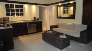 A modern kitchen with dark cabinetry, a built-in dishwasher, and a coffee maker. There is a white sofa and a wicker coffee table in the living area. - Casa Opal vacation home, 5 min from the beach! (Noord)