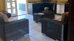 A bright kitchen with yellow walls, a microwave, stove, and a dishwasher. There are wicker chairs and a table in the living area. - Casa Opal vacation home, 5 min from the beach! (Noord)