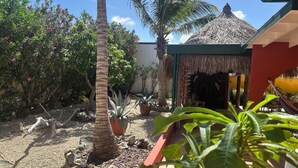 A tropical garden with palm trees, potted plants, and a thatched-roof structure. - Casa Opal vacation home, 5 min from the beach! (Noord)
