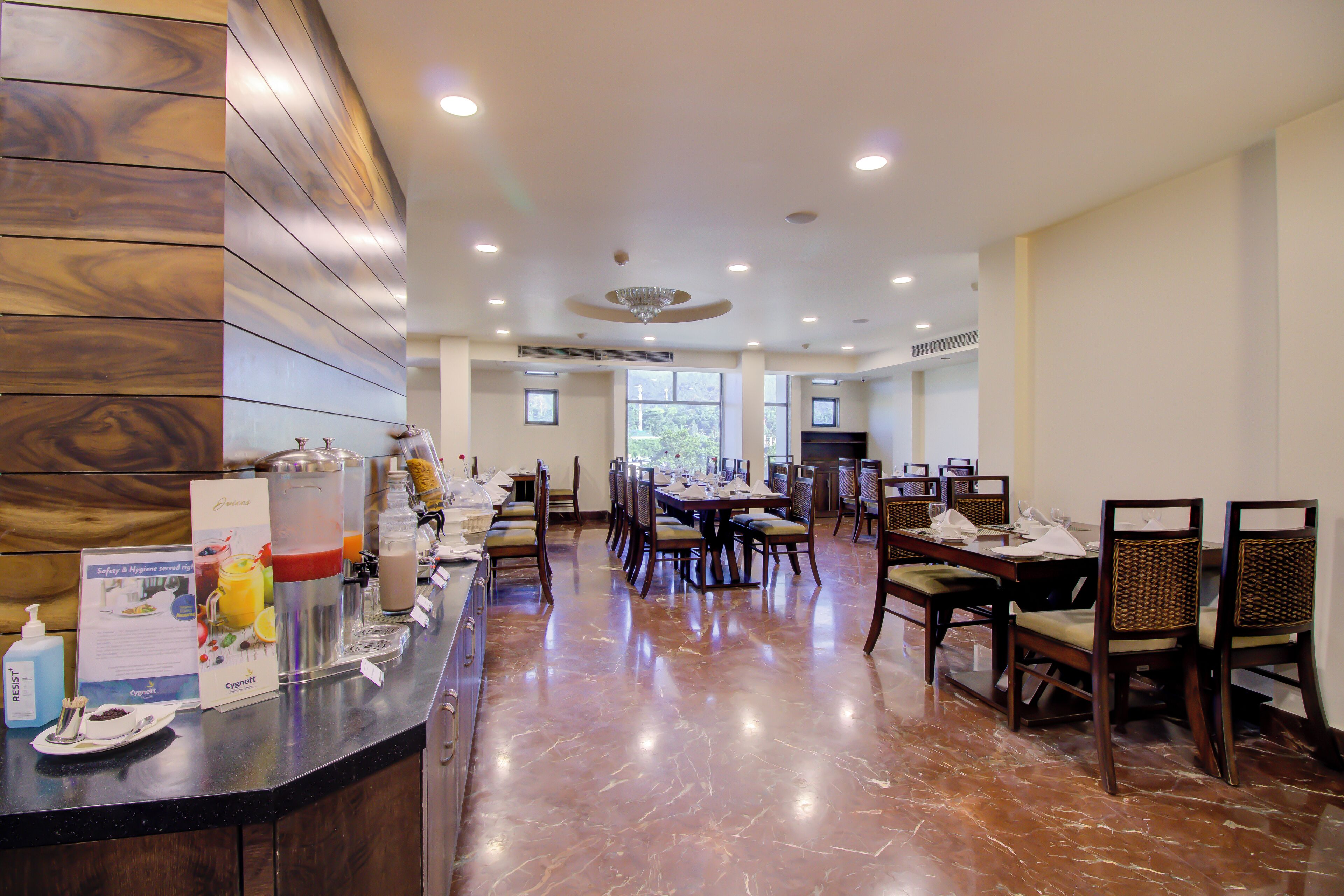 A hotel dining area with a marble floor, wooden paneling on one wall, and a buffet setup with various food items and beverages.