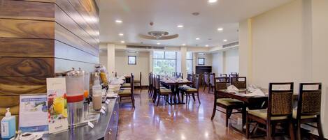 A hotel dining area with a marble floor, wooden paneling on one wall, and a buffet setup with various food items and beverages.