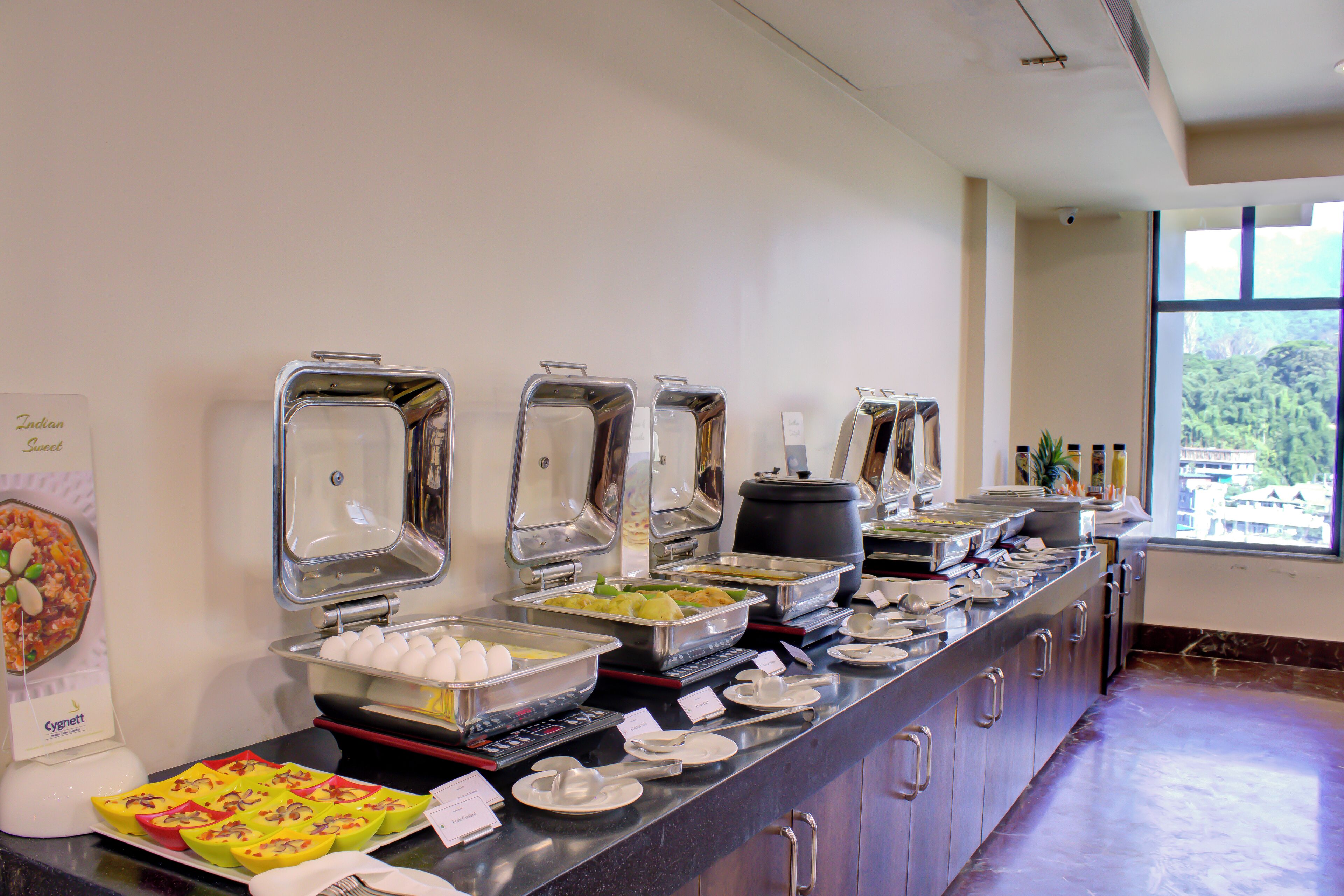 Un buffet avec différents stands de nourriture, notamment un plateau de fruits et un récipient d’œufs.