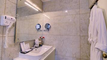 A bathroom with a white sink, a hairdryer, two mirrors, and a robe hanging on a door.
