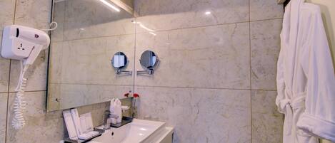 A bathroom with a white sink, a hairdryer, two mirrors, and a robe hanging on a door.