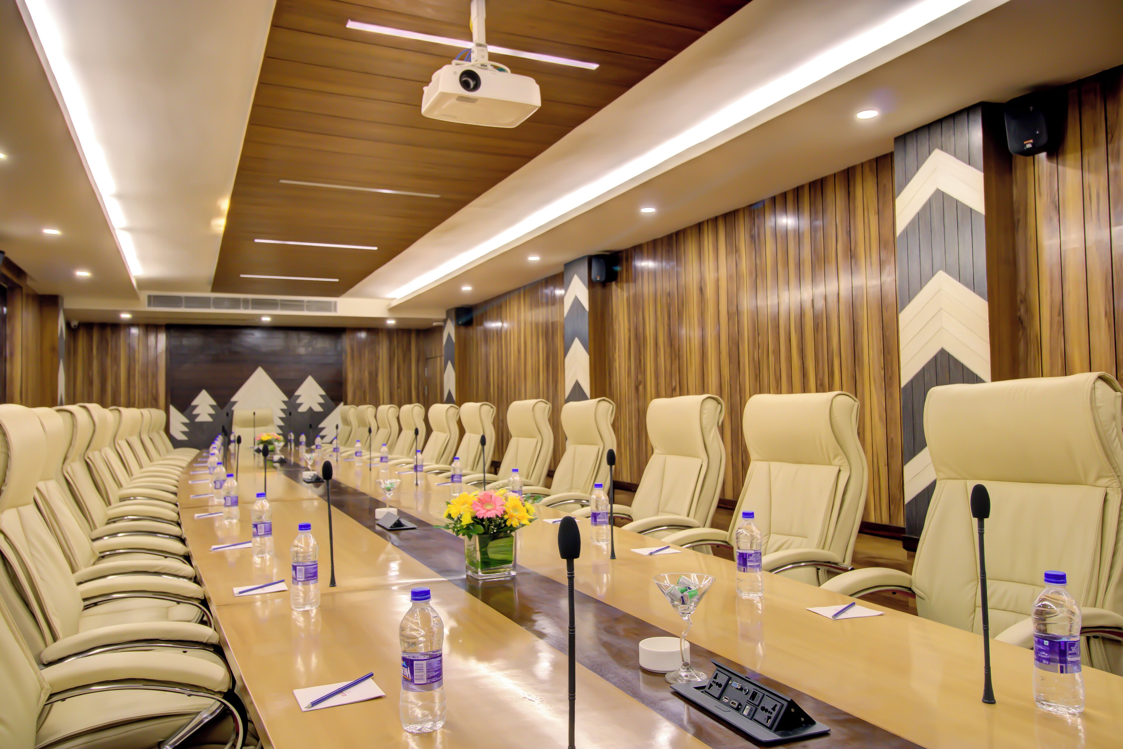 A conference room with a long table, multiple chairs, microphones, water bottles, and a projector.
