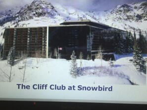 A modern building with a flat roof and large windows, surrounded by snow and trees. - Snowbird Cliff Club Sat. Dec 19, 2026 till Tue. Dec. 26, 2026 Pinnacle Platinum (Snowbird)
