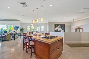 A modern kitchen with a central island, pendant lighting, and a dining area with chairs. - A 5-Star Estate, Large Groups, Luxury Living (Kihei)