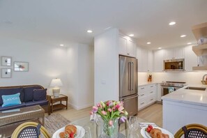 A modern kitchen with a refrigerator, oven, and microwave. There is a dining table with plates and glasses, and a sofa with a cushion.