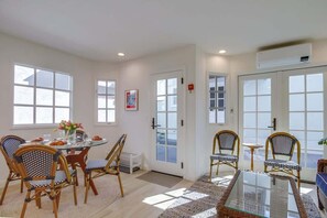 A spacious room with a dining table, wicker chairs, a glass-top coffee table, and large windows.